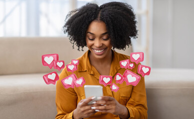 A young black woman with curly hair is sitting at home and smiling while checking her smartphone. She is surrounded by pink heart icons, indicating that she is receiving many likes