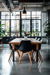 Fototapeta premium A spacious and light-filled dining room with a wooden table, black chairs, and large windows offering a view outside.