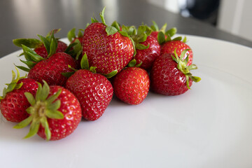 Strawberries on a white plate on a dark kitchen countertop