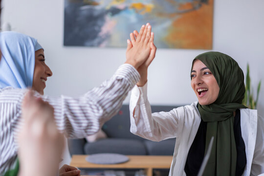 Three women in hijabs high-five each other in a modern office They are celebrating a success, highlighting teamwork and a positive work environment