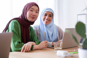 Two women in hijabs work together on laptops in a modern office They are deeply focused on their project showcasing teamwork and dedication