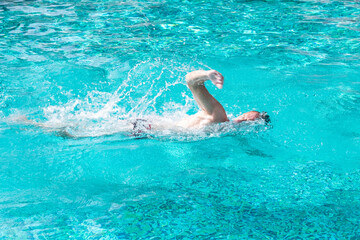 Mature active man swimming freestyle in outdoor swimming pool under the sun. Healthy lifestyle and sport concept