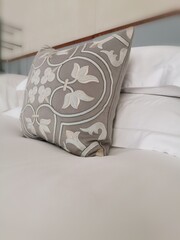 Gray decorative pillow stands on a white made bed