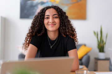A woman wearing headphones and using a smartphone while working on a laptop. This image showcases a focused and modern workspace, integrating technology for efficiency.