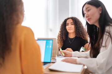 A group of colleagues in a brainstorming session, exchanging ideas and taking notes with laptops and documents on the table in a modern office space