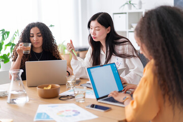 A diverse group of young professionals engaged in a collaborative team meeting, discussing ideas with laptops and documents on the table in a bright, modern office
