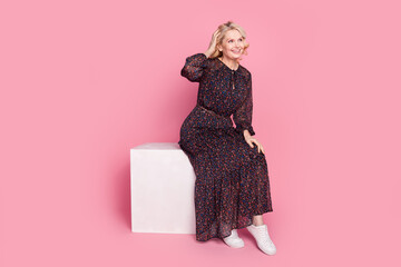 Full length portrait of nice aged lady sit podium look empty space wear dress isolated on pink...
