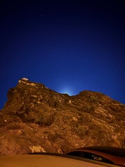 Photograph of the moon shining behind a rock at the sea in Mijas, Spain