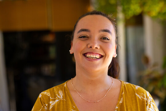 Smiling woman in yellow shirt enjoying time at home, looking at camera