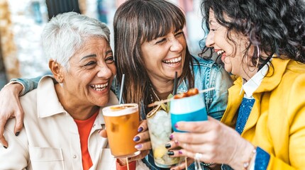 Happy senior women drinking cocktail glasses sitting at bar table - Group of best friends enjoying happy hour cheering drinks at pub restaurant - Life style concept with girls hanging out together