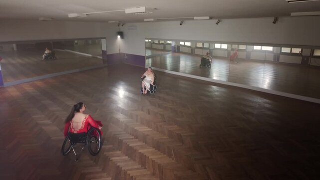 Two women, skilled professional wheelchair dancers in a rehearsal for the competition, training in a dance studio in front of mirrors, high angle shot.