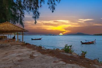 Colourful Skies Sunset over Rawai Beach in Phuket island Thailand. Lovely turquoise blue waters, lush green mountains colourful skies and beautiful views of long tail Boats