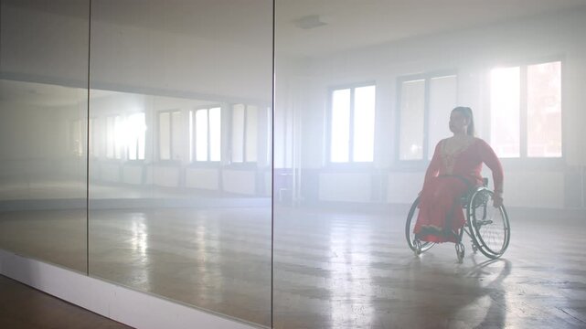 Beautiful long-haired woman with a disability in a ballroom red dress, reflected in the mirror in the empty dance room, side view. Para dancing concept.