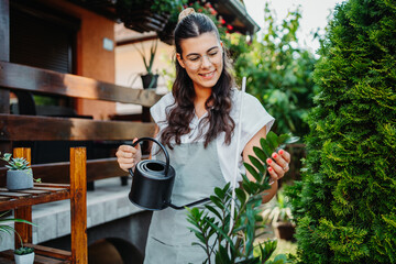 Young woman taking care of plants with water can and mister