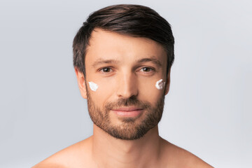 Obraz premium Male Skincare. Handsome Mature Man Applying Face Cream On Skin Over White Studio Background.