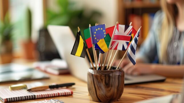 Close-up of international flags on a desk, with a blurred woman foreign language teacher working at a laptop, Foreign language online course, class, e-education concept.