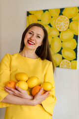 Obraz premium girl in a yellow dress holds lemons and oranges in her hands
