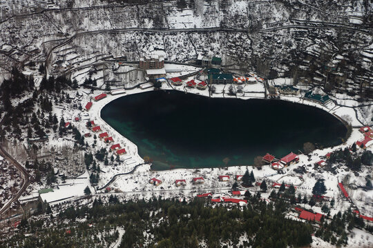 Aerial view of snowy village with lake, mountains, and trees, Skardu, Gilgit-Baltistan, Pakistan.