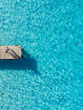 Aerial view of crystal clear waters with two people and a turtle at wooden pier, Westpunt, Curacao.