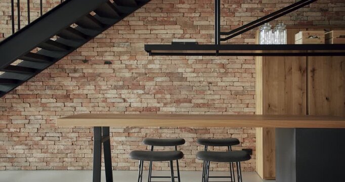 Modern and spacious wooden kitchen room with wall bricks and black staircase. Real Estate. Luxury kitchen with wooden island and chairs. Real Luxury Design Interior. Neoclassic Style, cozy interior.