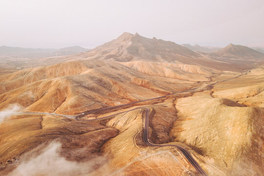 Aerial view of remote and barren mountains and hills with road and clouds, Mirador Astronomico de Sicasumbre, Fuerteventura, Spain.