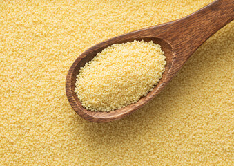Yellow raw organic healthy couscous grain seeds on wooden spoon textured background.Macro.