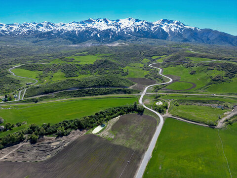 Aerial view of green fields, winding roads, and snow capped mountains in valley, Peterson, Utah, United States.