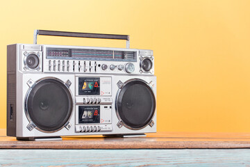 Boombox radio stereo cassette recorder on vintage wooden shelf front yellow background. Retro old...