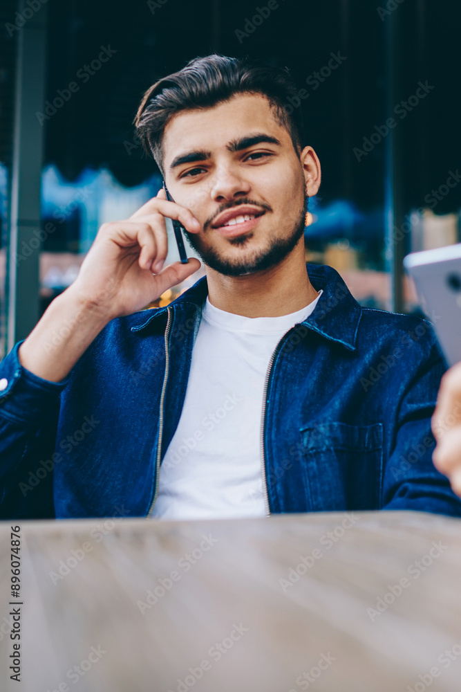 Poster portrait of handsome male talking on mobile phone and looking at camera while her girlfriend using s