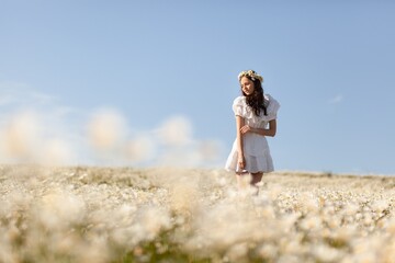 Beautiful girl with chamomile flowers walking in field