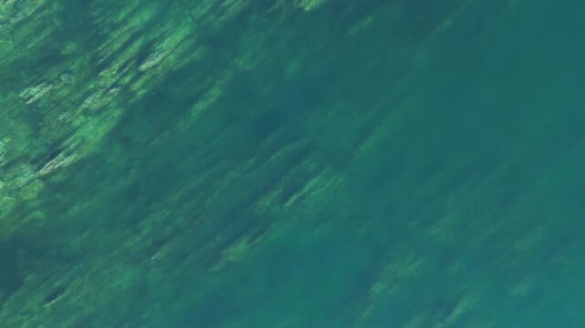 Aerial view in Monteferro, Nigr&aacute;n, capturing rugged coastal rocks submerged in turquoise waters. The camera starts close to the water, gradually ascending to reveal more of the coastal landscape.