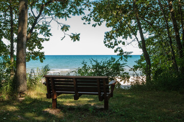 A shaded park bench affords a visitor an overlooking view of the calm waters of Lake Michigan from Harrington Beach State Park, Belgium, Wisconsin in early July.