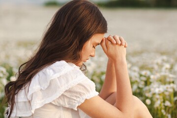 Woman praying on nature chamomile field background.