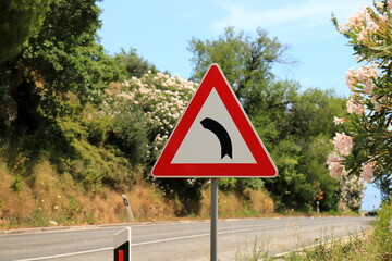 Road sign Dangerous left turn on a mountain road in Croatia. Curving road, triangular warning road sign