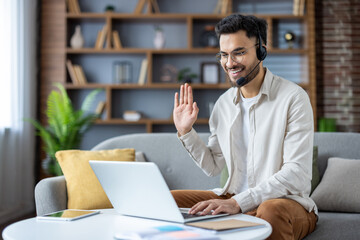 Young man working from home on laptop during online video conference call. smiling and waving