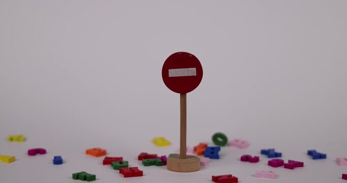 Wooden "No Entry" sign with colorful letters falling from above, representing learning difficulties. The white background emphasizes the visual metaphor. In slow motion
