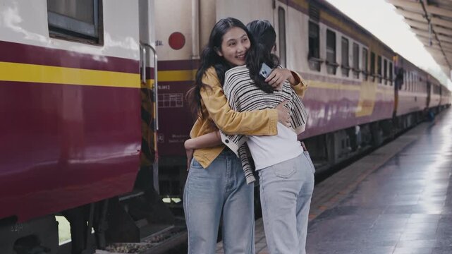 Two friends reunite on a train platform, sharing a heartfelt hug and joyful smiles