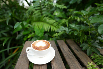 White Cappuccino coffee cup and spoon on wooden table with green tropical plants in garden