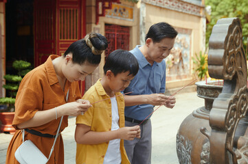 Fototapeta premium Family of three using aroma sticks while praying near the ancient sculpture