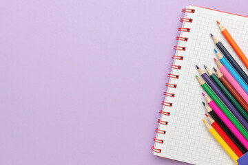 Colorful Pencils on Spiral Notebook with Grid Paper on a Purple Background