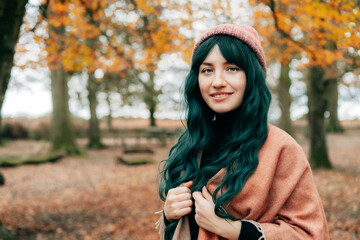 Woman in hat wrapped in warm Shawl Poncho enjoying autumn walk in forest with fall yellow leaves. Travel lifestyle. Feeling harmony, reunion with nature. Relaxing, personal fulfillment. Local travel