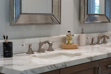 Detail of sleek double bathroom sinks with white swirl pattern countertop, chrome faucets with glass handles, dark wood cabinets and silver finish mirrors.