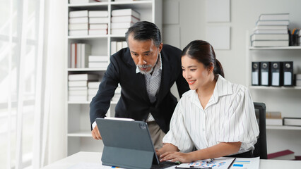 Senior manager is showing something on a tablet to a younger female employee in an office setting