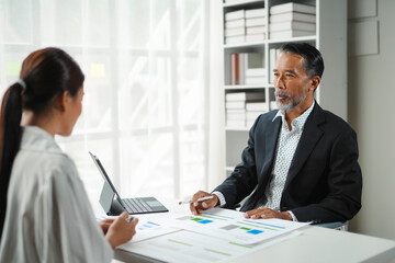 Senior executive gestures towards an analytics report while discussing a business strategy with a coworker