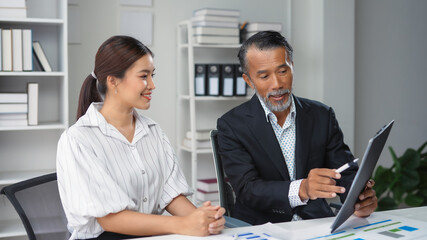 Experienced manager presenting marketing data on digital tablet to young colleague in modern office setting