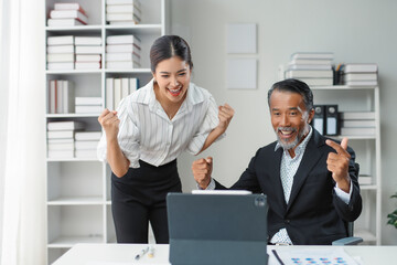 Businessman and businesswoman celebrate their success as they review a digital tablet in the office