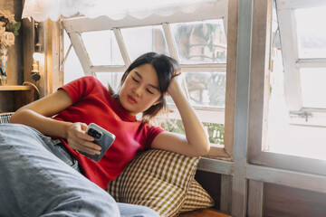 Asian woman lie down to take a rest and checking out mobile phone in the house.