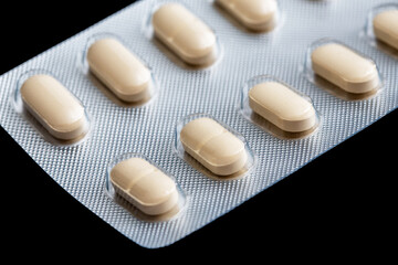 Metal tablet blister. Yellow pills medicine. Silver shiny blister with drugs. Creamy color capsules isolated on black. Empty copy space health texture. Illegal drug market. Aluminum pills blister.