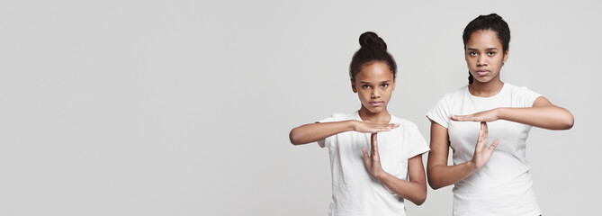 Beautiful african teenaged girls showing time out sign over grey studio background