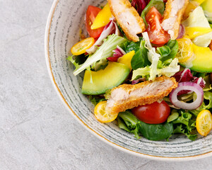 Salad with chicken, avocado, mango, cherry tomatoes, lettuce, onion removal, kumquat, on a gray background.